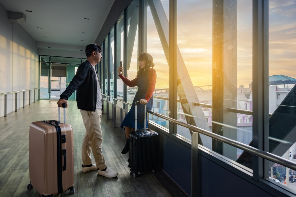 Cool,Traveling,Offer.,Asian,Couple,Traveler,With,Suitcases,Using,Smartphone